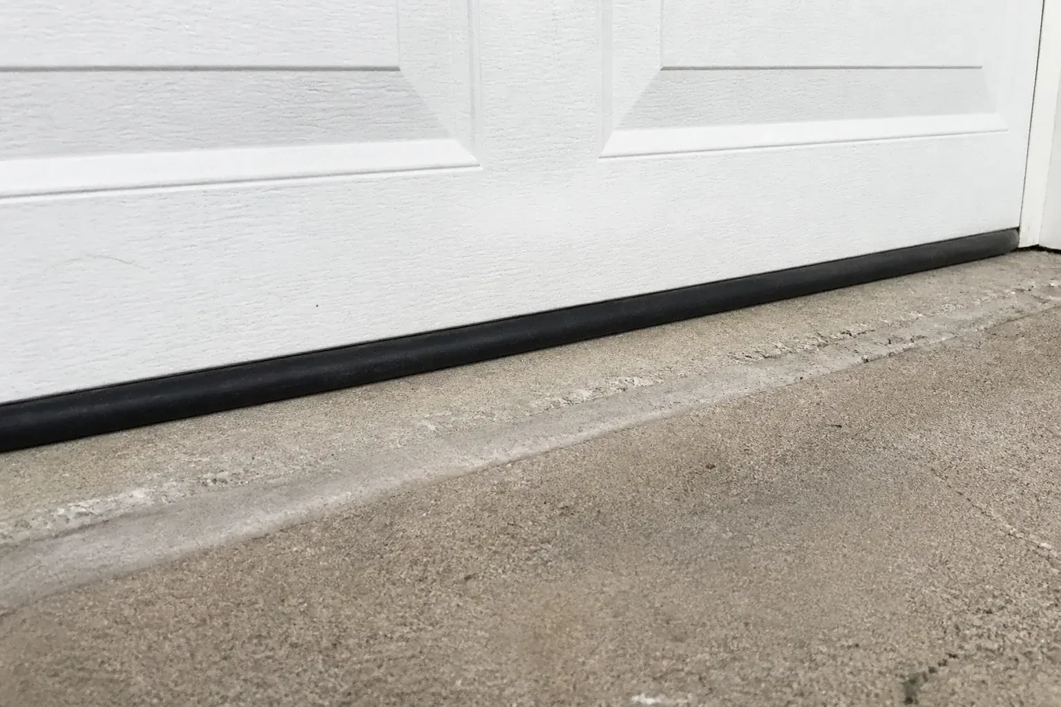 Black bottom seal along a closed white garage door at a concrete threshold. — Garage Door Bottom Seal Replacement, Oakville