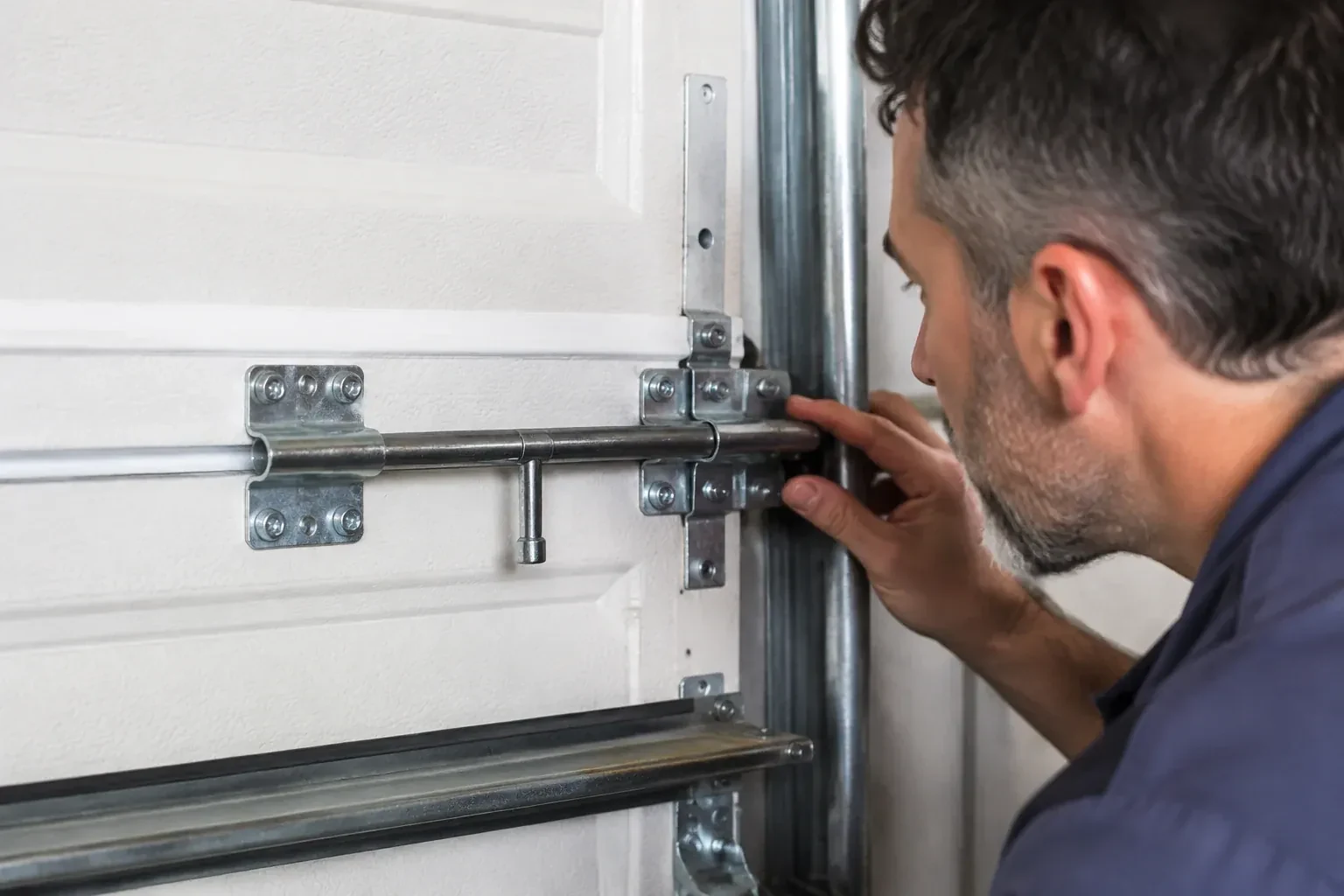 Person leaning close to a white paneled door, one hand on a metal slide-bolt bar mounted across the panel. — Garage Door Manual Lock Repair, Oakville