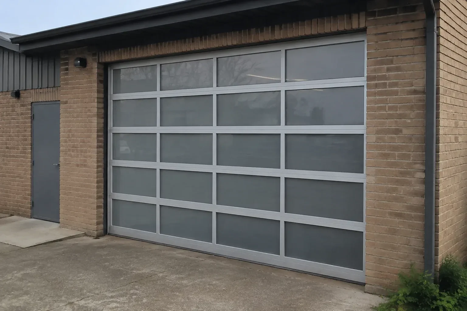 Closed glazed sectional door in a grey metal frame at a brick workshop. — Full-View Glass Garage Door Installation, Oakville