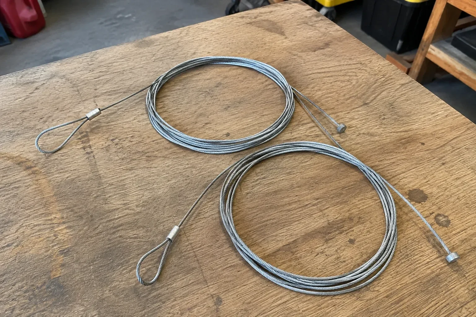 Two coiled steel cables with loop and stop ends on a workbench. — Garage Door Cable Replacement, Bronte